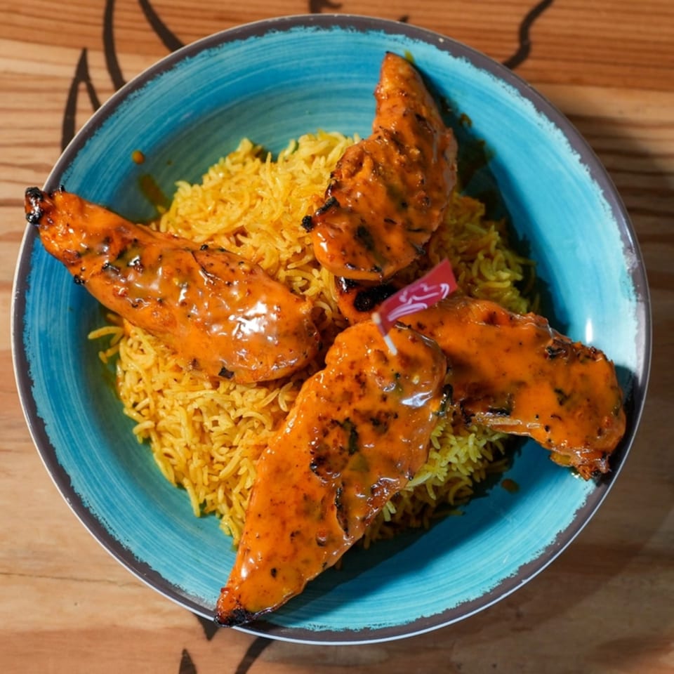 Four peri-peri chicken tenders arranged on a bed of yellow rice in a blue bowl.