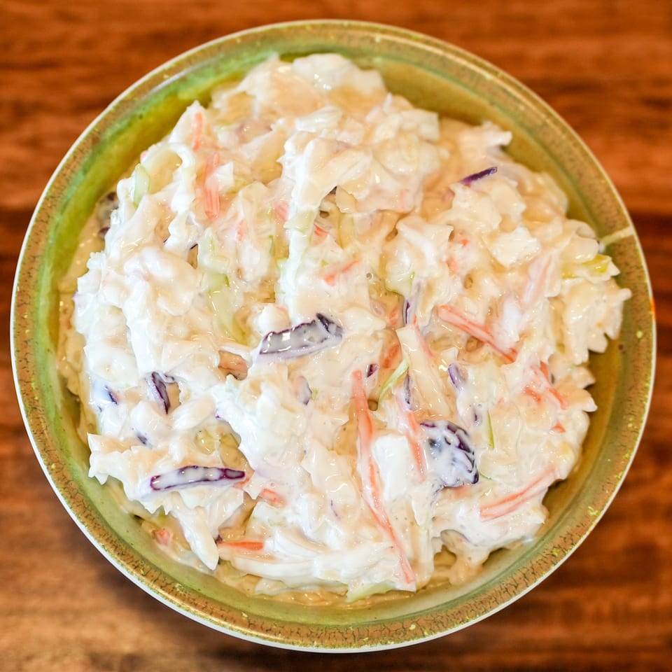 Creamy coleslaw with shredded cabbage and carrots in a green bowl on a wooden table.