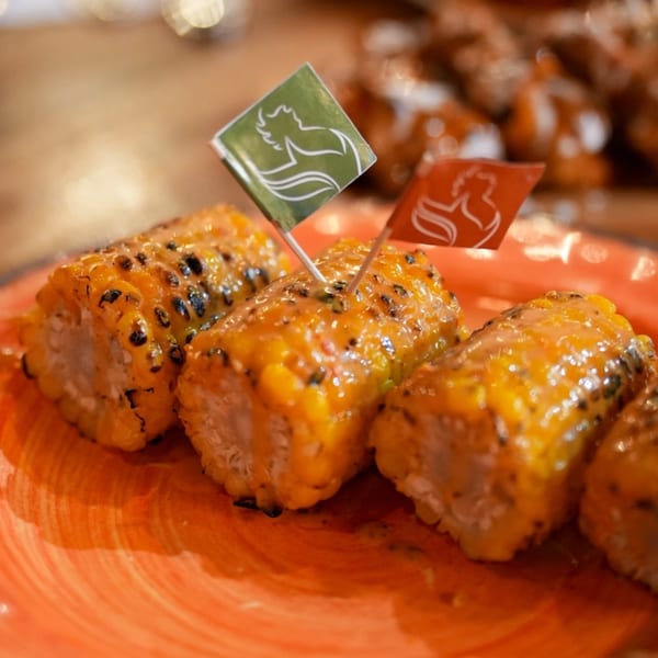 Grilled corn on the cob pieces with sauce and two small flags on an orange plate.