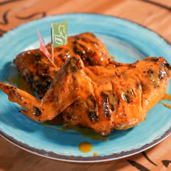 Two pieces of peri-peri chicken on a blue plate, garnished with small flags.