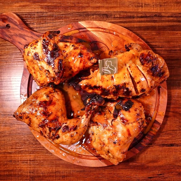 Four pieces of grilled peri-peri chicken with sauce on a wooden serving board.