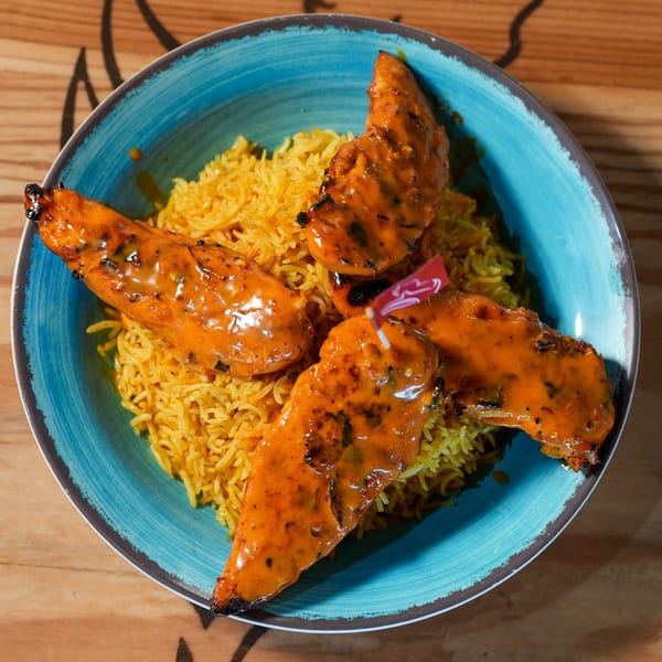 Four peri-peri chicken tenders with rice in a blue bowl on a wooden table.