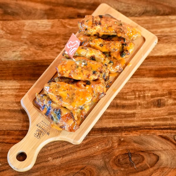 Peri-peri chicken wings covered in a creamy orange sauce, served on a wooden board.