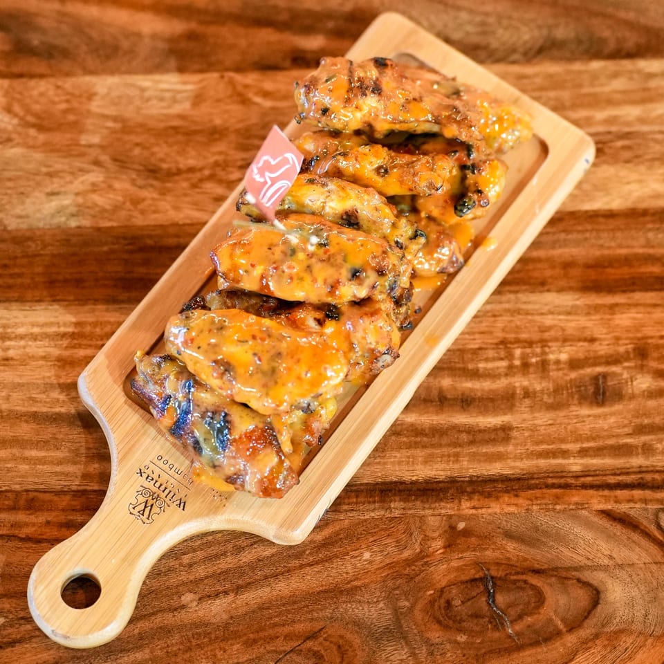 Peri-peri chicken wings covered in a creamy orange sauce, served on a wooden board.
