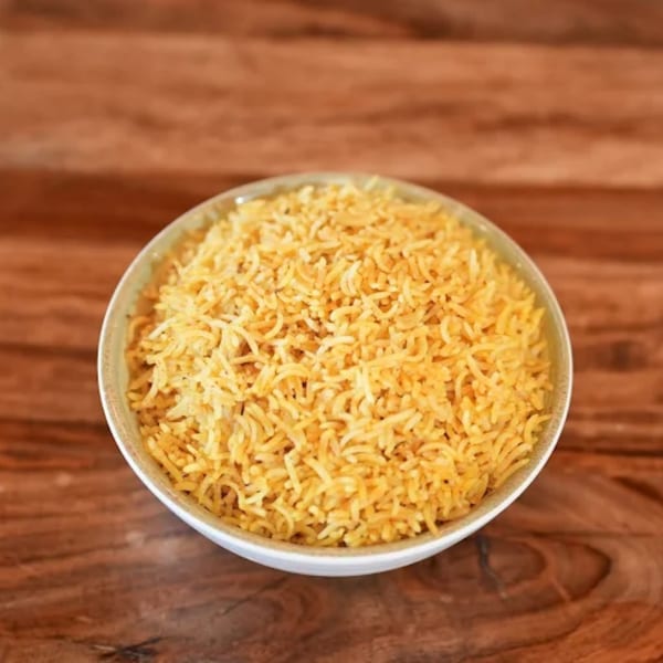 A white bowl filled with golden yellow rice sits on a rustic wooden table.