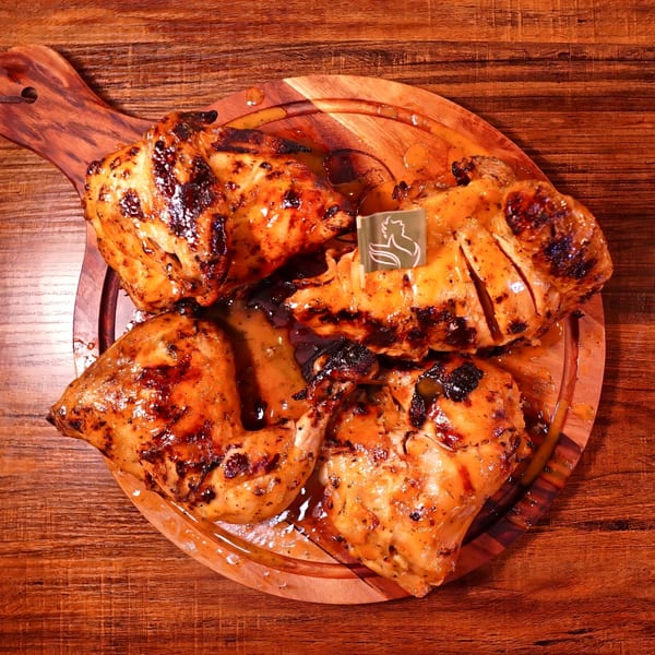 Four pieces of glistening, grilled peri-peri chicken on a wooden serving board.