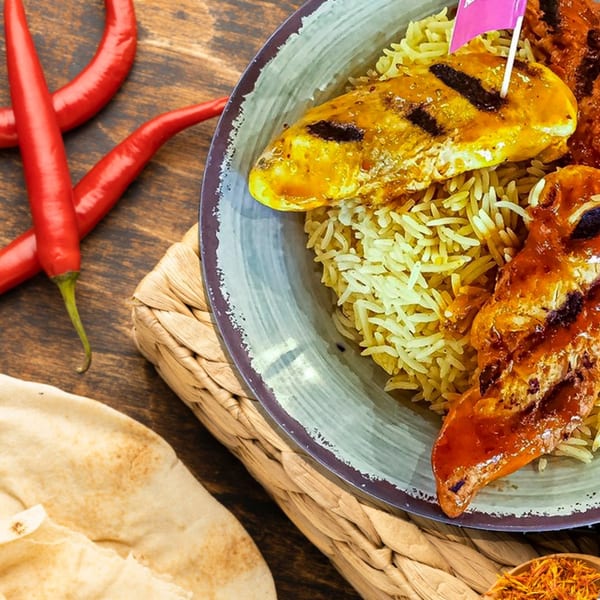 Peri-peri chicken with rice, flatbread, red chilies, and saffron on a wooden table.